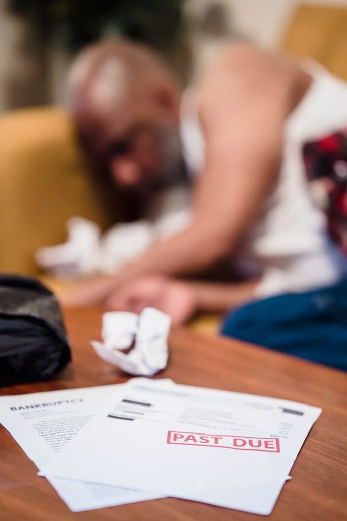 Depressed man lying near overdue bill notices indicating financial stress and bankruptcy.